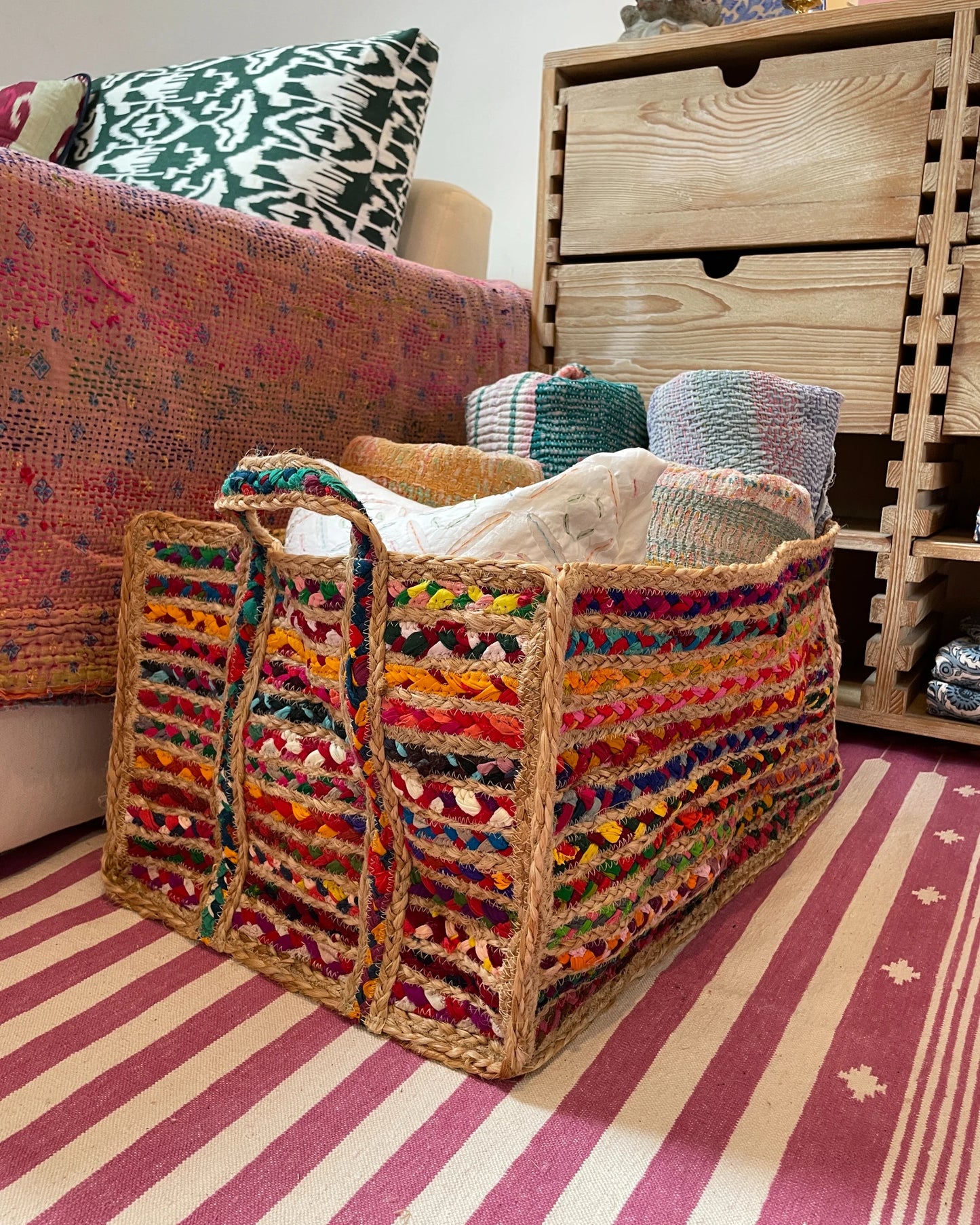 Colorful woven storage basket on a striped rug filled with blankets for storage
