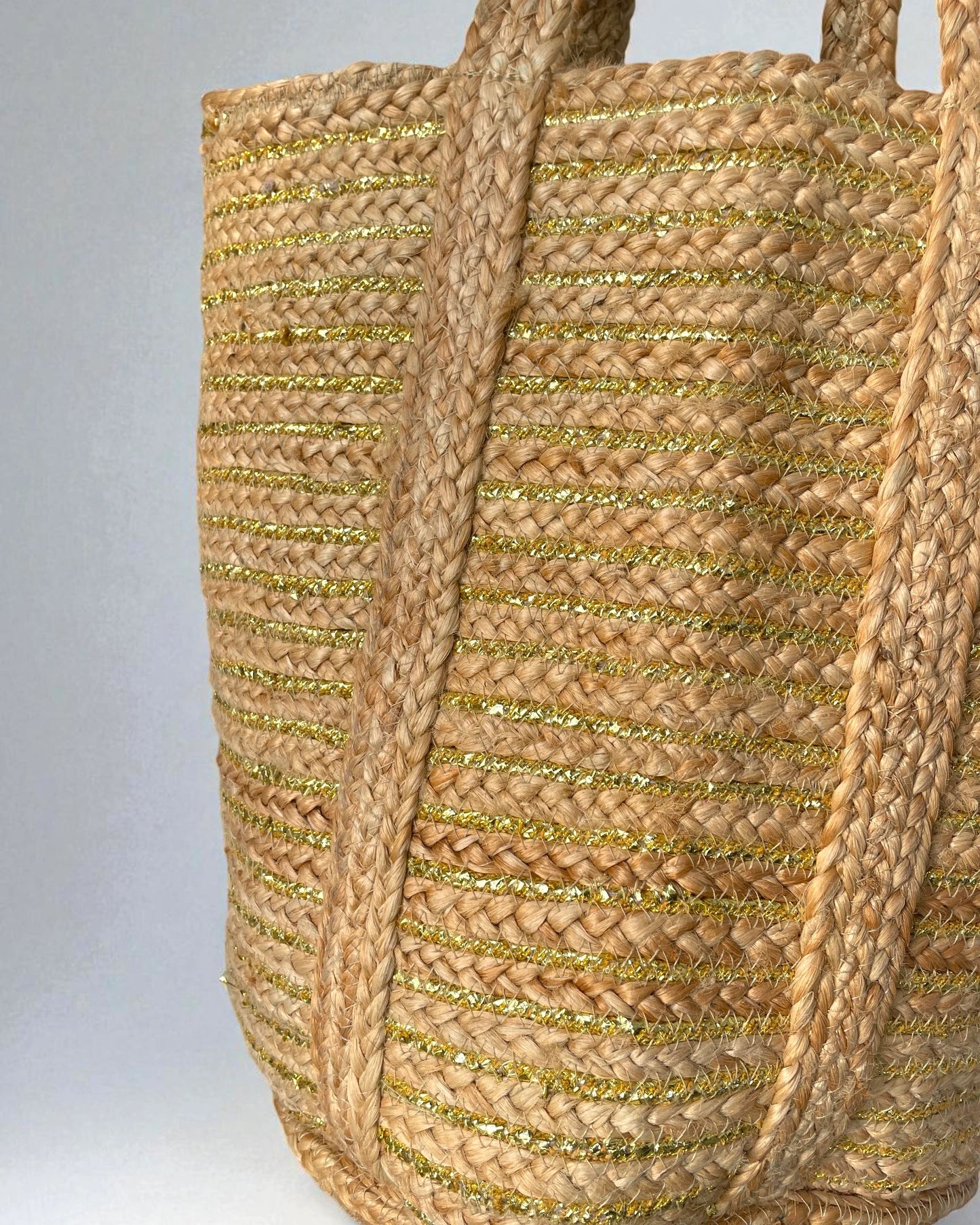Woven large jute shopper bag with gold accents on a gray background