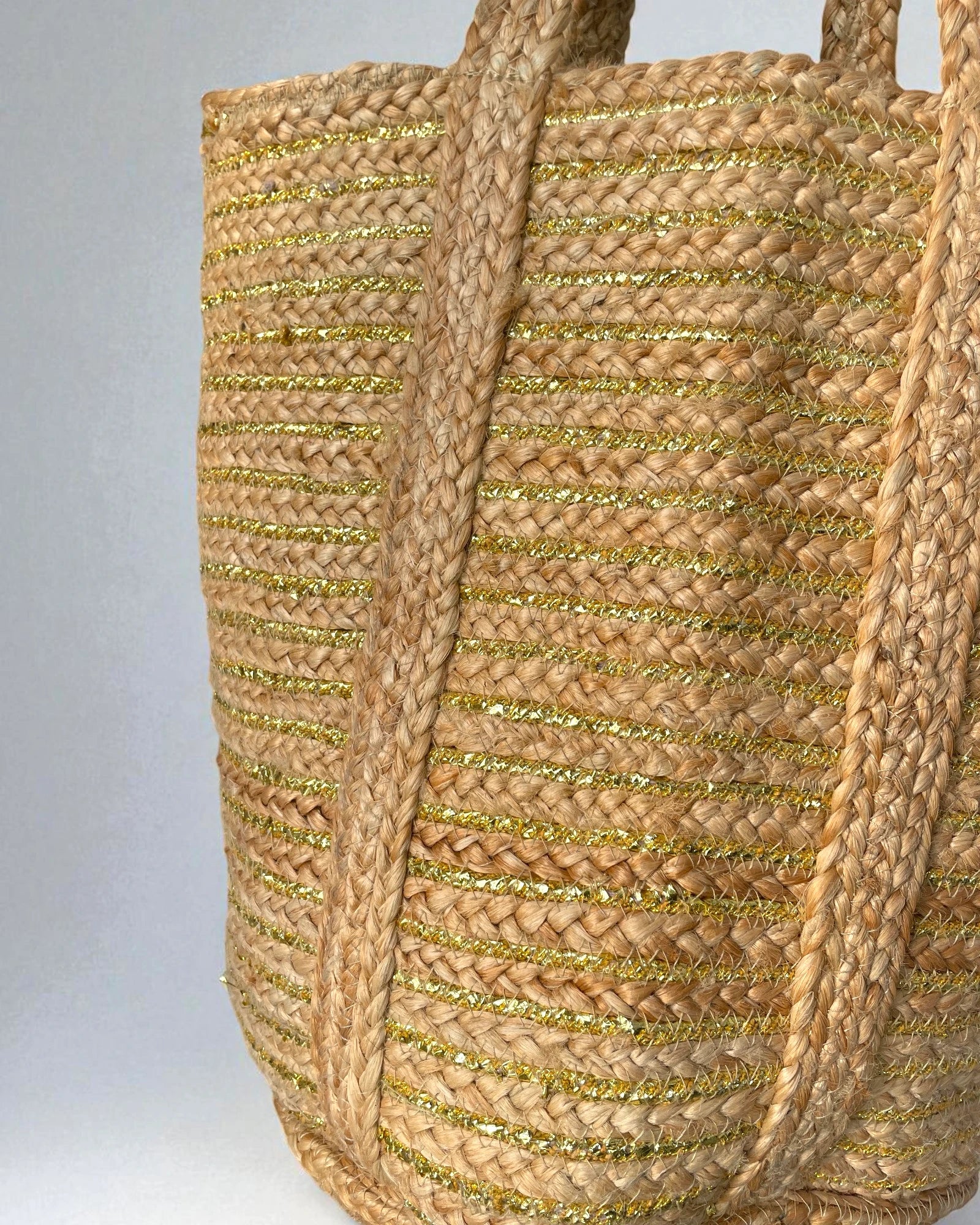 Woven large jute shopper bag with gold accents on a gray background