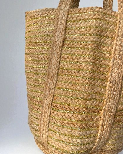Woven large jute shopper bag with gold accents on a gray background