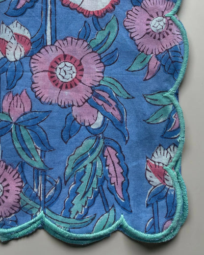 Set of six scalloped-edge cotton napkins with pink floral print on a sky blue background and teal trim
