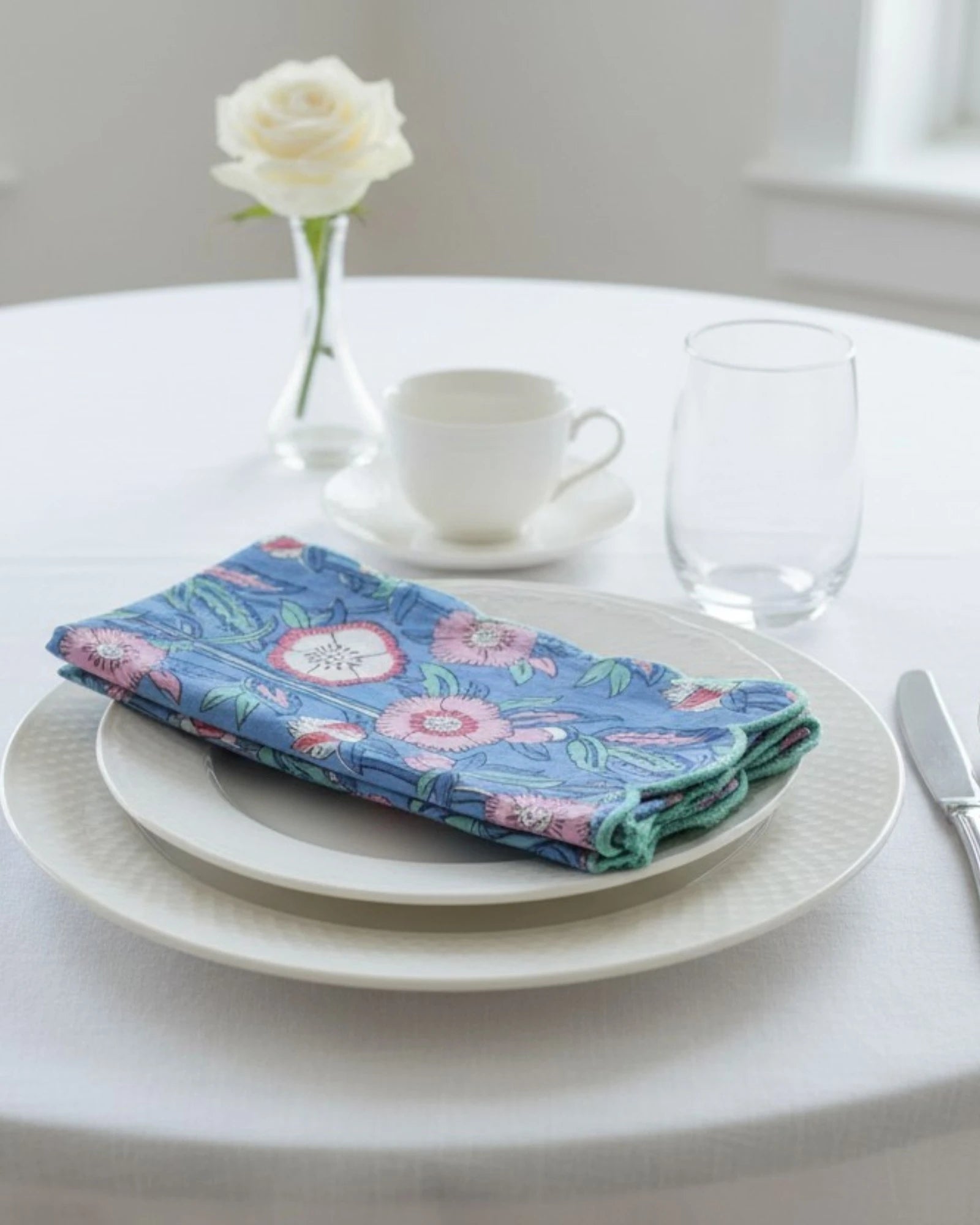 Handmade cotton table napkins featuring a pink floral pattern on sky blue fabric with decorative scalloped edging