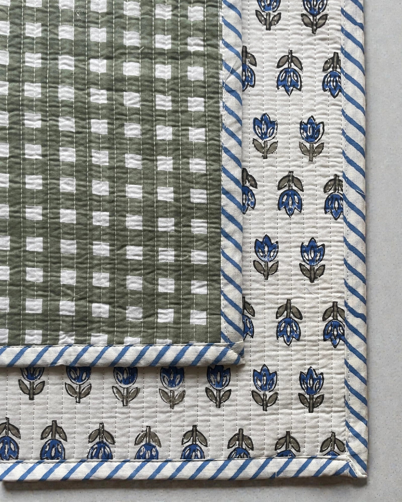 Reversible quilted placemats featuring blue floral motifs with green geometric border and striped edging.