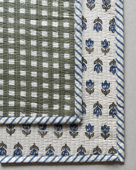 Reversible quilted placemats featuring blue floral motifs with green geometric border and striped edging.
