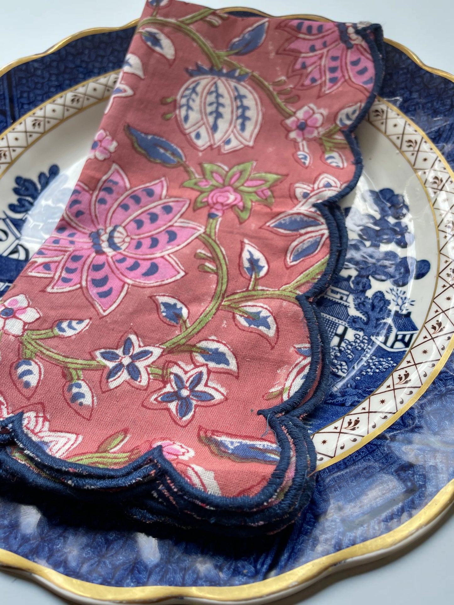 Set of six reusable cotton napkins with a muted red design and decorative navy scalloped border