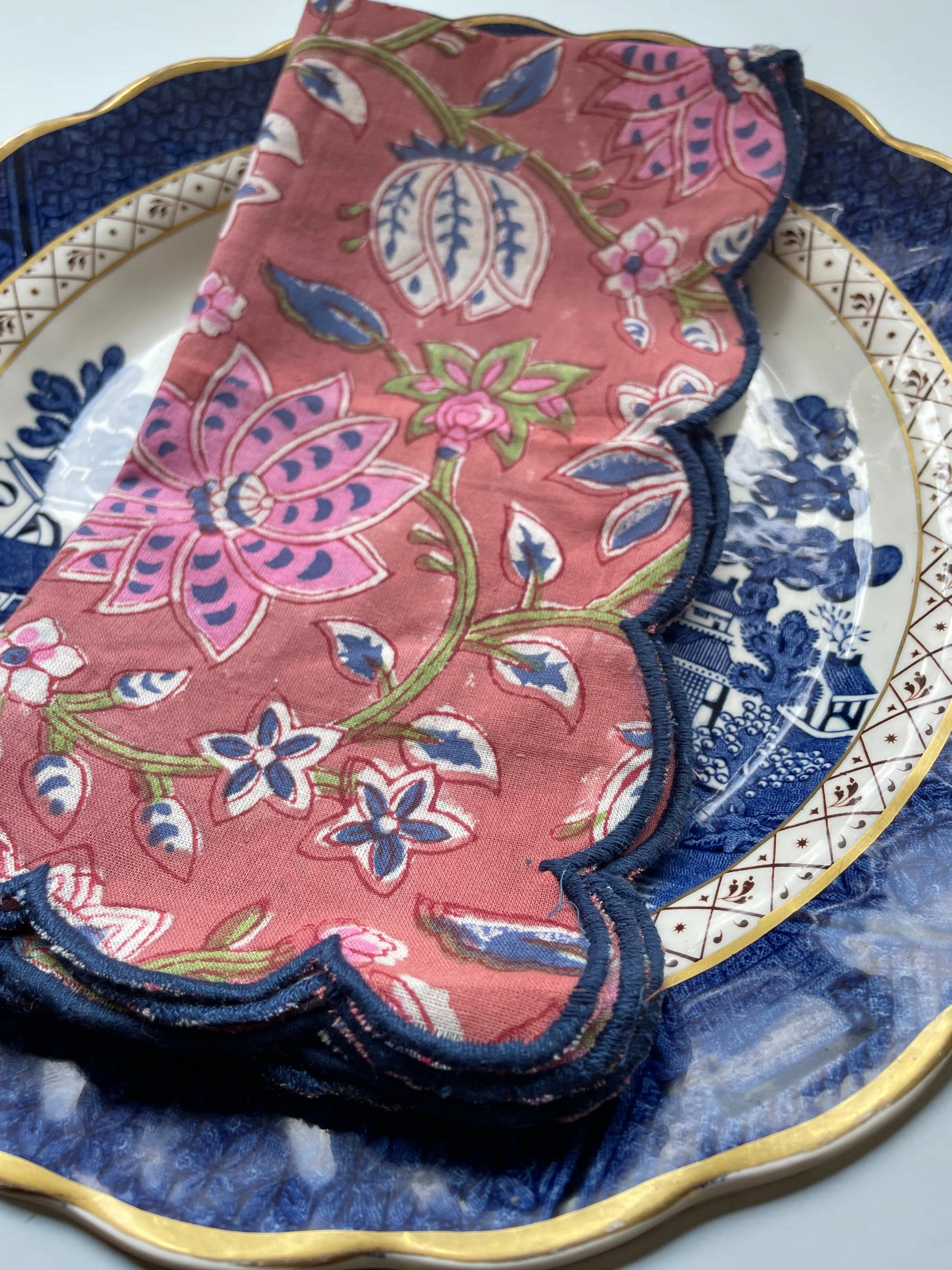 Set of six reusable cotton napkins with a muted red design and decorative navy scalloped border