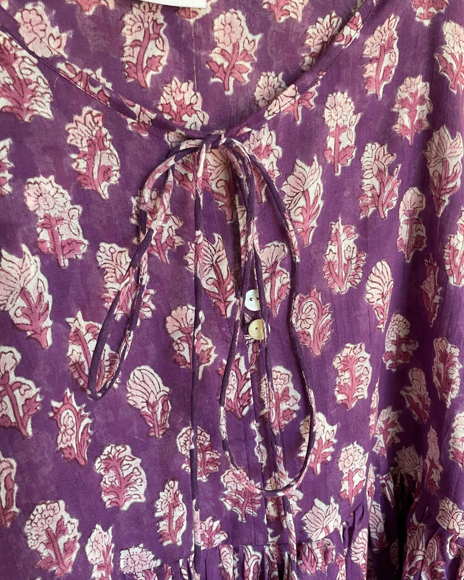 Close-up of the tie neckline and hand block printed cotton fabric  with mother of pearl buttons on the Amethyst mini dress